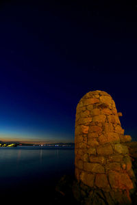 Illuminated rock by sea against clear sky at night