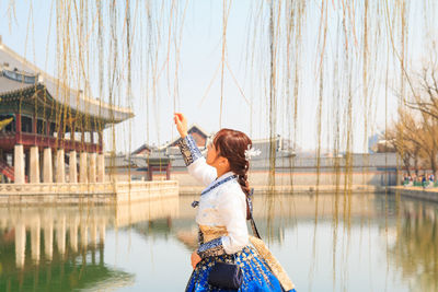 Young woman touching vines over pond against sky