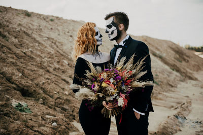 A couple in love celebrates halloween in costumes and makeup with a bouquet of dried flowers