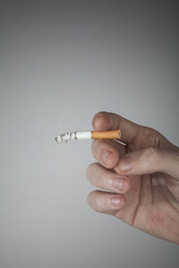 Close-up of hand holding cigarette over white background