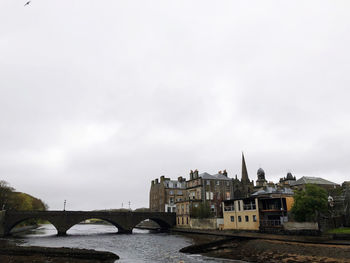 Bridge over river by buildings against sky