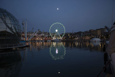 Illuminated ferris wheel by river against sky at night