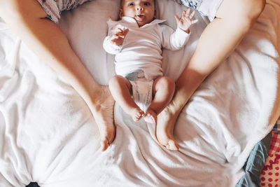 Top view of crop newborn baby in diaper lying on bed with mother in house