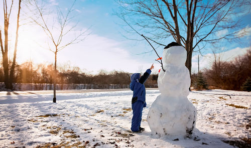 Little boy pointing to snowman on sunny day