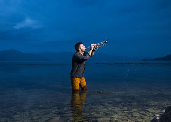 Young man playing musical instrument in sea at dusk