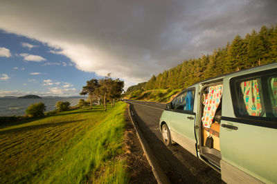 Car on road amidst field against sky