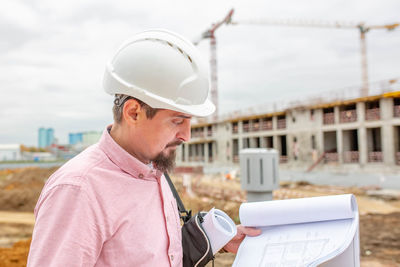 Man holding mobile phone while standing at construction site