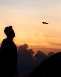 Silhouette man watching airplane flying against sky during sunset