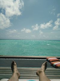 Low section of person relaxing by sea against sky