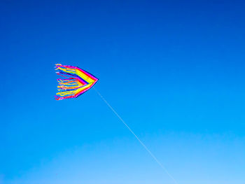 Low angle view of colorful kite flying in clear blue sky