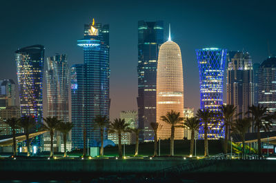 Illuminated doha tower and modern buildings against clear sky