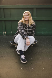 Portrait of smiling teenage girl sitting on skateboard