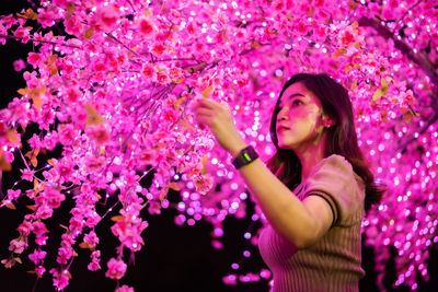 Beautiful woman standing against illuminated tree at night