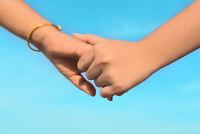 Close-up of hand holding hands against blue sky