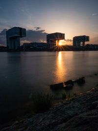 Buildings by sea against sky during sunset in city