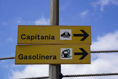 Low angle view of  road sign pointing direction of police and gas station in spanish language 