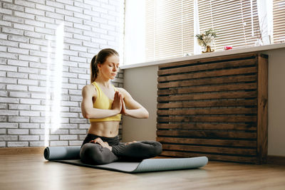 Young woman sitting on wooden floor against wall