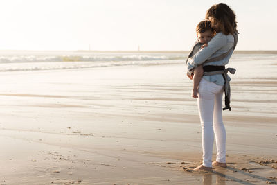 Mother carrying son while standing at beach