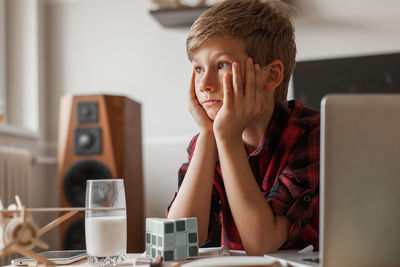 Pensive boy thinking of something with head in his hands at home.