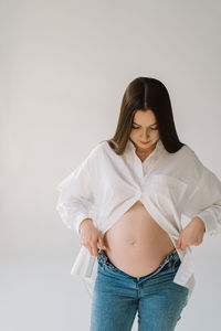 Cute young pregnant girl sitting on the white studio in warm light