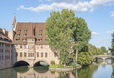 Arch bridge over river by buildings against sky