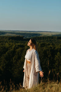 Young woman meditating and catching sunlight outdoors at sunset with scenic landscape