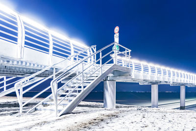 Low angle view of illuminated bridge over sea against clear blue sky at night