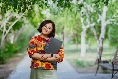 Confident young professional woman with laptop in summer city park