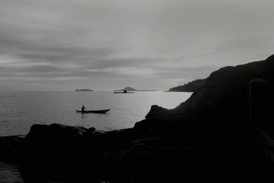 Silhouette person on rock by sea against sky