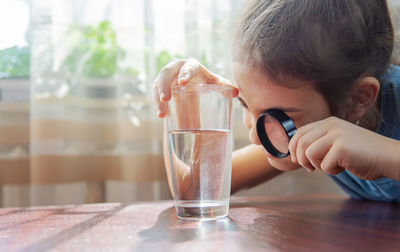 Girl looking at water through magnifying glass at home