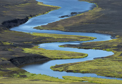 From above of picturesque landscape of bright blue river flowing among volcanic terrain in iceland