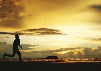 Silhouette boy playing on beach against sky during sunset