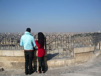 Rear view of friends standing on retaining wall against clear sky