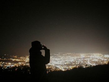 Silhouette of woman photographing illuminated city at night