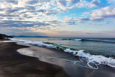 Scenic view of sea with crashing waves against dramatic sky during sunrise