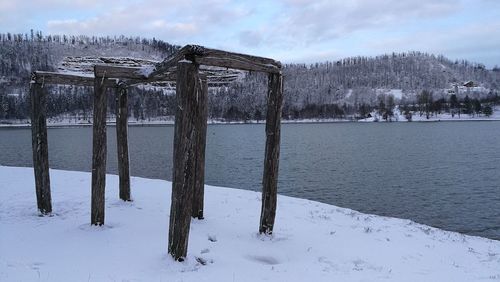 Wooden posts on frozen lake against sky during winter