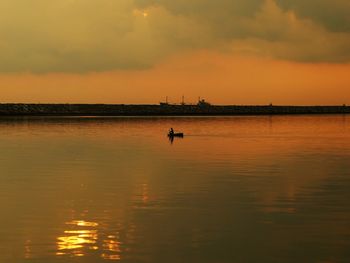 Man rowing boat in lake against sky during sunset