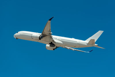 Low angle view of airplane flying against clear blue sky