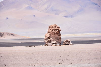 Rock formation on sand at beach against sky