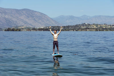 Shirtless man paddleboarding in sea against mountains
