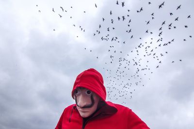 Low angle view of woman flying birds against sky