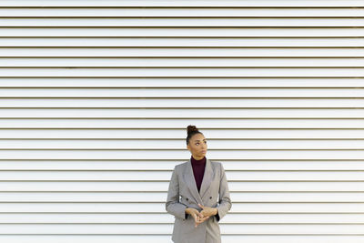 Thoughtful businesswoman looking away while standing against striped wall