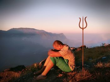 Men sitting on mountain against sky during sunset