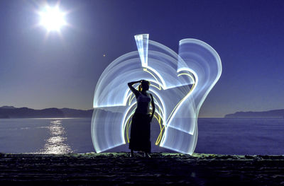 Woman standing at illuminated shore against sky at night