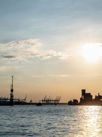 Silhouette of commercial dock by sea against sky during sunset