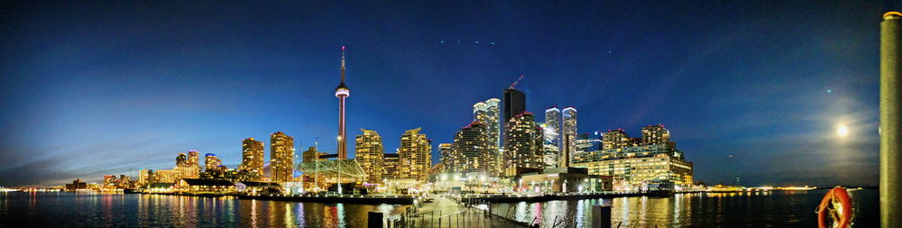 Panoramic view of illuminated buildings by river against sky at night