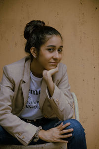 Portrait of young woman sitting on seat against wall