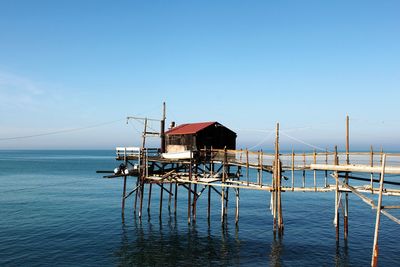 Stilt house on pier by sea against clear blue sky
