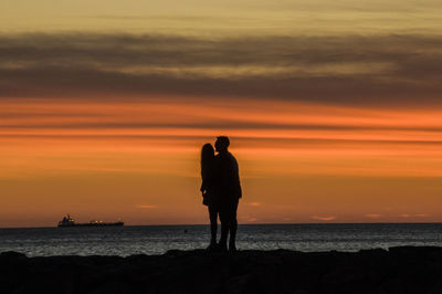 Silhouette man standing by sea against orange sky