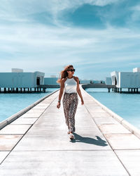 Full length of woman standing by swimming pool against sky